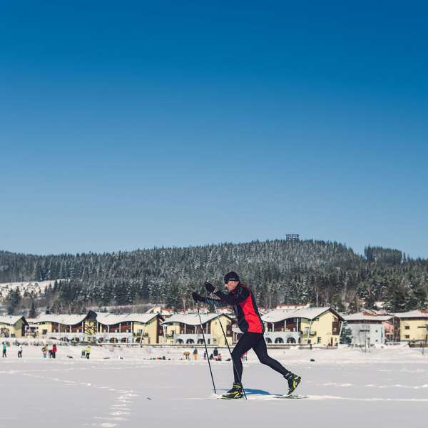 Běžkař v pozadí s lidmi na lipenské magistrále a apartmány Marina Lipno