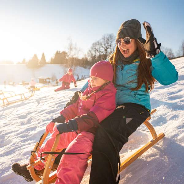 Maminka s holčičkou sjíždějí kopec na saních