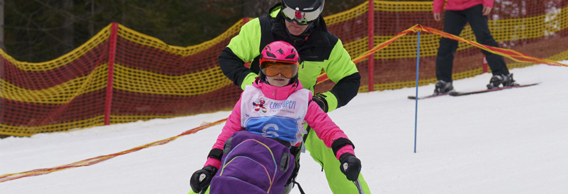 Handikepovaný lyžař na monoski lyžuje s asistentem