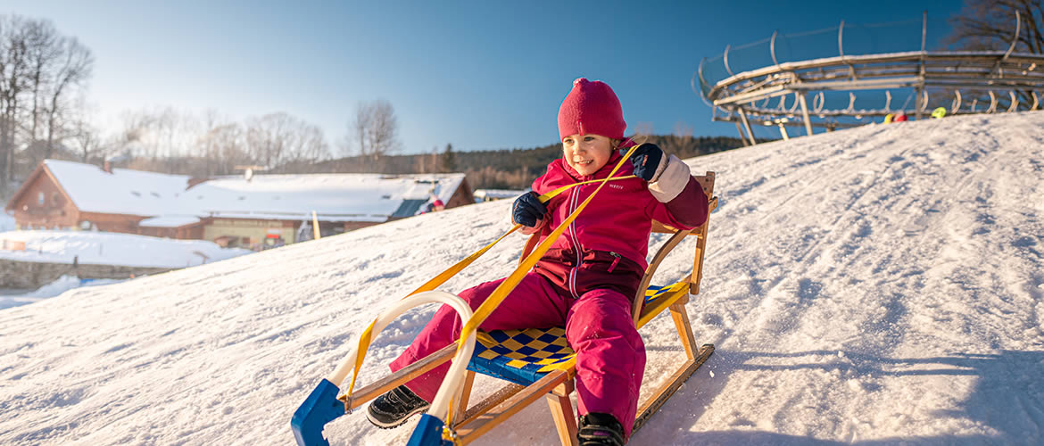 Holčička sáňkuje na kopci u bobové dráhy Lipno